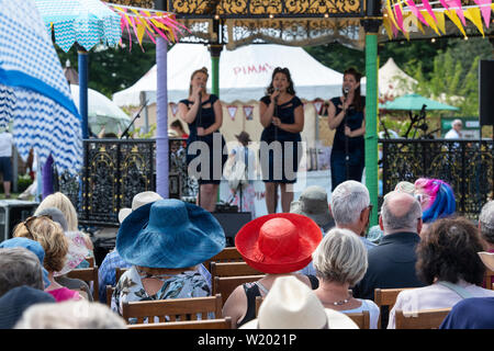 Leute saßen auf Stühlen, einen weiblichen Vintage boogie - woogie Gesangsgruppe im musikpavillon an der RHS Hampton Court Flower Show 2019. Surrey, England Stockfoto