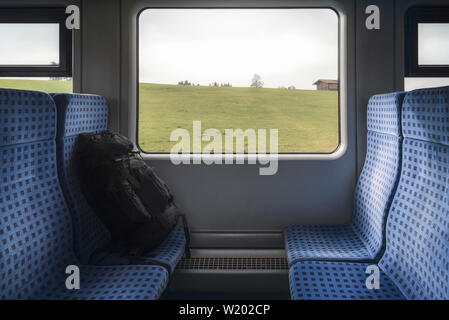 Reisen in Deutschland mit einem deutschen Regionalbahn Innenraum, blaue Stühle, schwarzer Rucksack, und Fenster mit Blick in die Natur. Stockfoto