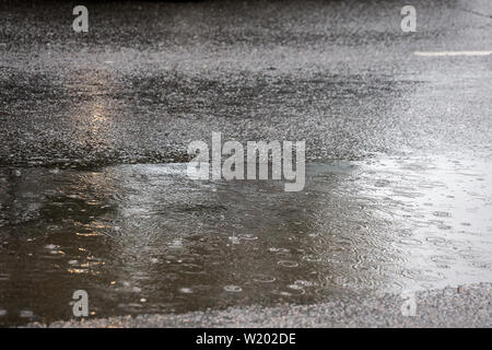 Pfütze auf Asphaltstraße bei Tageslicht Regen in der Stadt mit selektiven Fokus und Boke verwischen. Stockfoto