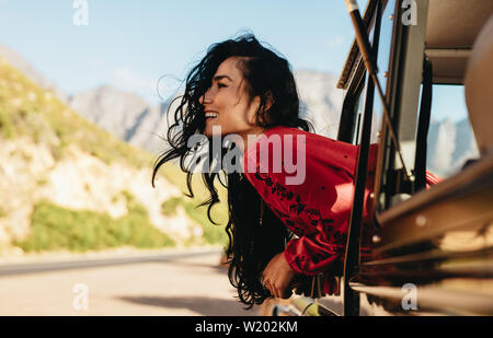 Schöne kaukasische Frau suchen aus dem Auto und lächelnd auf Road Trip. Frau Spaß zu haben, während sie von einem Auto unterwegs. Stockfoto
