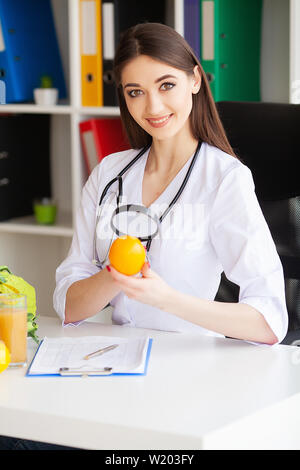Gesundheit. Arzt Dietologist hält an der frischen Orange Hände. Gesunde Ernährung. Frisches Obst und Gemüse auf den Tisch. Gerne Arzt im Licht Stockfoto