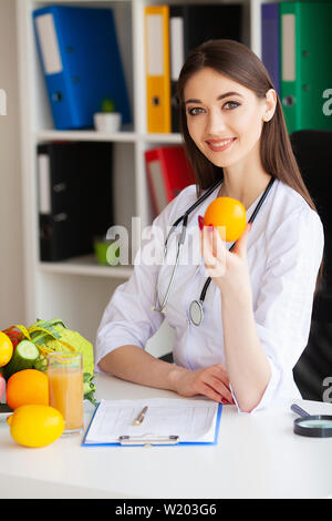 Gesundheit. Arzt Dietologist hält an der frischen Orange Hände. Gesunde Ernährung. Frisches Obst und Gemüse auf den Tisch. Gerne Arzt im Licht Stockfoto