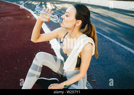 Junge Frau mit einer Flasche Wasser nach dem Joggen im Freien in Singapur. Sie trägt Grau top und eine leichte Sport Leggings Stockfoto