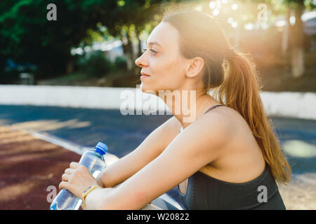 Junge Frau mit einer Flasche Wasser nach dem Joggen im Freien in Singapur. Sie trägt Grau top und eine leichte Sport Leggings Stockfoto