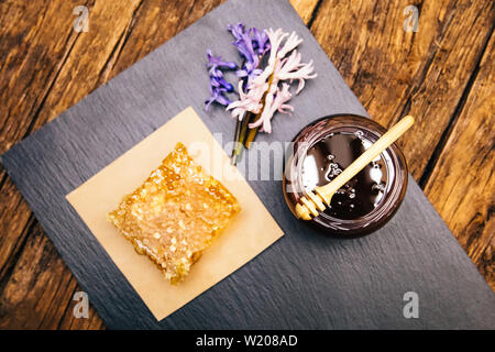 Gesunde, natürliche, organische und süßen Honig im Glas oder Schüssel mit Honig Pendelarm, Blumen und Wabe auf schwarzem Hintergrund. Stockfoto