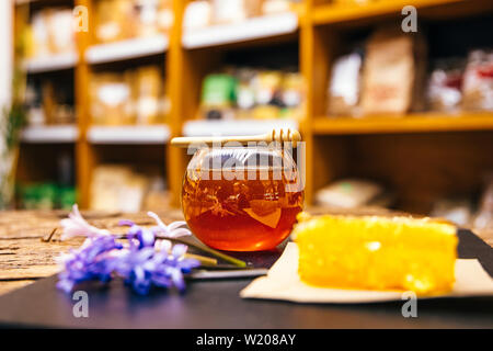 Gesunde, natürliche, organische und süßen Honig im Glas oder Schüssel mit Honig Pendelarm, Blumen und Wabe auf schwarzem Hintergrund. Stockfoto