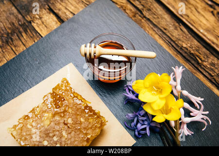 Gesunde, natürliche, organische und süßen Honig im Glas oder Schüssel mit Honig Pendelarm, Blumen und Wabe auf schwarzem Hintergrund. Stockfoto