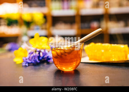 Gesunde, natürliche, organische und süßen Honig im Glas oder Schüssel mit Honig Pendelarm, Blumen und Wabe auf schwarzem Hintergrund. Stockfoto