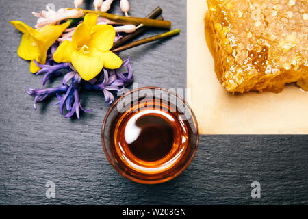 Gesunde, natürliche, organische und süßen Honig im Glas oder Schüssel mit Honig Pendelarm, Blumen und Wabe auf schwarzem Hintergrund. Stockfoto