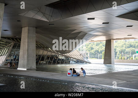 04 Juli 2019, Frankreich (Frankreich), Lyon: Besucher sitzen unter dem Museumsbau des 'Musée des Confluences". Foto: Sebastian Gollnow/dpa Stockfoto