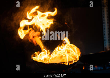 Asiatische Koch Holding flaming Wok in einer Garküche Stockfoto