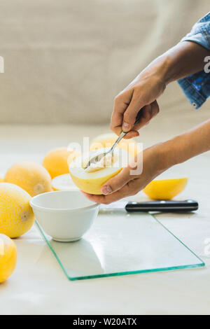 Reife melone Beeren auf eine helle Küche Tisch, in die Hände von einem halben Melone, mit einem Löffel Samen gereinigt. saisonale Sommer Früchte Stockfoto