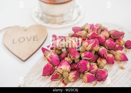 Chinesischer Tee mit rosa Blüten. Tea Rose Knospen von real Rosenknospen, gezupften Junge und dann getrocknet. Eine Tasse Tee und ein Holz- Herzen mit den Worten ich Lo Stockfoto