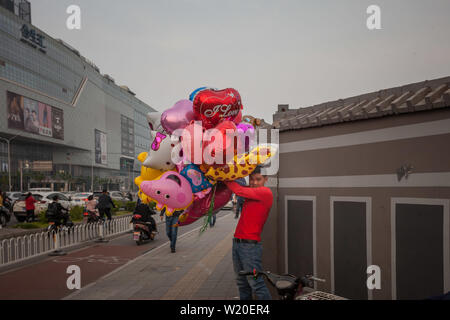 Junger Mann verkaufen bunte Ballone während der Stosszeiten auf dawang Straße und Guang Qu Straße Kreuzung - Peking, China Stockfoto