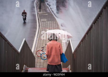 Mädchen gehen hinunter zum Fuß-Brücke während der regnerischen Tag in Peking Stockfoto