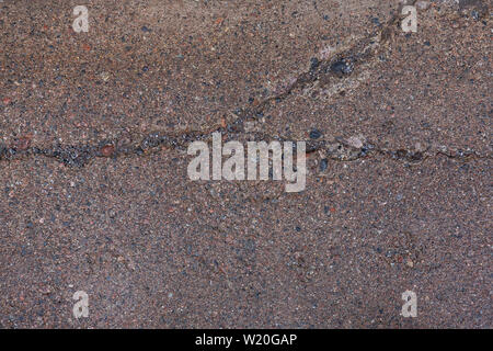 Nahaufnahme eines nassen, verwitterte und gerissenen Beton Fußweg Oberfläche mit Kieselsteinen (oder pebblecrete oder freiliegenden Aggregat) im Freien, von oben gesehen. Stockfoto