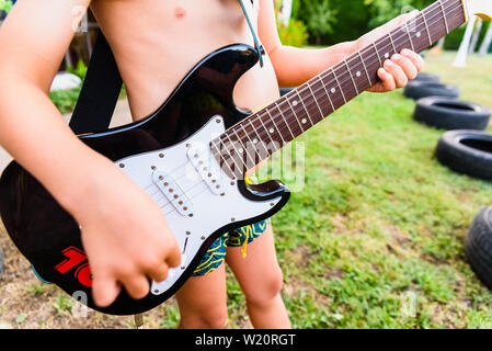 Detail einer E-Gitarre, die ein Kind in seinem Hinterhof auf seine Sommerferien statt. Stockfoto