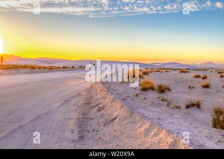 Road Trip In Die Wüste. Wunderschöner Sonnenuntergang in der Wüste mit abgelegener Landstraße, die sich durch die Sanddünen des White Sands National Monument in New Mexico schlängelt Stockfoto