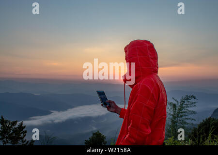 Mann mit Handy auf dem Berg mit der Sonne und Nebel. Stockfoto