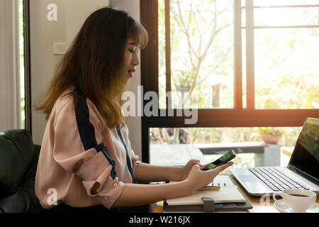 Schöne junge geschäftsfrau mit Handy beim Sitzen vor dem Laptop im Home Office. Stockfoto