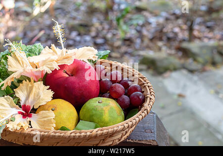 Apfel-, Orangen- und Traubensaft in Leinwandbindung Bambuskörben mit Blumenschmuck Hintergrund verschwommen Bäume. Stockfoto