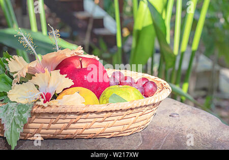 Apfel-, Orangen- und Traubensaft in Leinwandbindung Bambuskörben mit Blumenschmuck Hintergrund verschwommen Bäume. Stockfoto