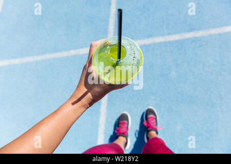 Läufer trinken ein gesunder Spinat grüne Smoothie im Freien Laufbahn vorbereiten. Nahaufnahme einer Hand, die Saft trinken auf Blue Lane, soziale Medien Gesundheit und Fitness Concept. Stockfoto