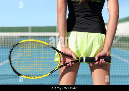 Tennis Player holding Schläger vorbereiten für das Spiel im Freien Gericht im Sommer. Nahaufnahme von Händen und Sport Rock mit Net im Hintergrund. Nicht erkennbare untere Körper der Person, von der Rückseite. Stockfoto