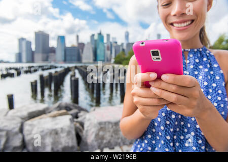 Sms Telefon Mädchen auf Sommer New York reisen aus Brooklyn Bridge Park Pier 1 Blick auf Downtown Manhattan. Nahaufnahme von pink Smartphone für Online Social Media. Asiatische Frau mit Technologie. Stockfoto