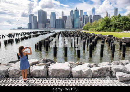 New York touristische Frau unter mobile Bild mit Smartphone. Manhattan Skyline der Stadt waterfront Lifestyle. Menschen zu Fuß genießen Aussicht auf die Innenstadt von der Brooklyn Bridge Park Pier 1 Salt Marsh. Stockfoto