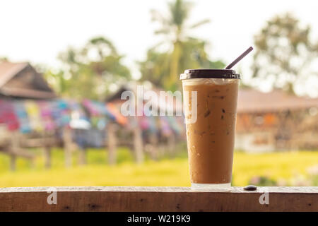 Eiskaffee auf dem Holzboden hinter einem Reisfeld und farbenfrohen Stoffen. Stockfoto