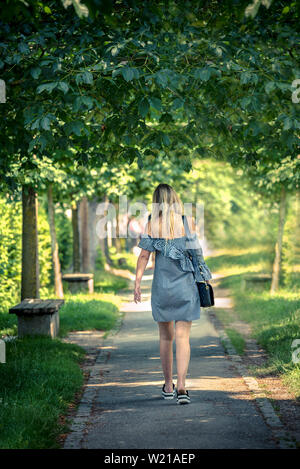 Langhaar blonde Schönheit Spaziergänge durch den Park auf dem Weg zur Arbeit. Einen schönen sonnigen Tag im Park. Stockfoto