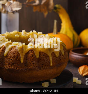Kürbis bundt Kuchen gekrönt mit Zucker Glasur und kandierten Früchte auf einem dunklen Holz- Board. Stockfoto