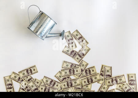 Gießen Sie Wasser aus der Gießkanne Banknoten Dollar auf einem weißen Hintergrund. Konzept, Investition, Start-up, Startup, Wachstum der Einkommen. Stockfoto