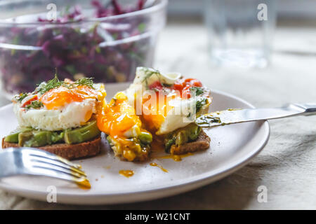 Frühstück serviert von zwei Toasts mit Avocado, Spiegelei mit Gemüse und Kräutern auf einem rustikal Tischdecke Hintergrund. Blick von oben. Gesunde und Nutr Stockfoto