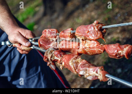 Mann hält in der Hand einen Spieß mit rohem Fleisch, Life Style. Stockfoto