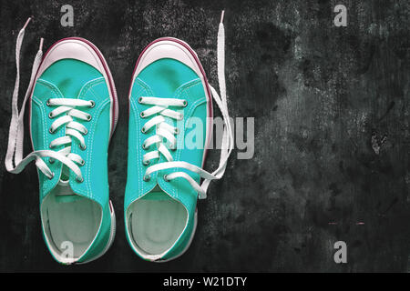 Blau - blaugrün - Grün - türkis Sneaker mit Ungebundener Schnürsenkel auf einem dunklen konkreten Hintergrund. Kopieren Sie Platz. Ansicht von oben Stockfoto