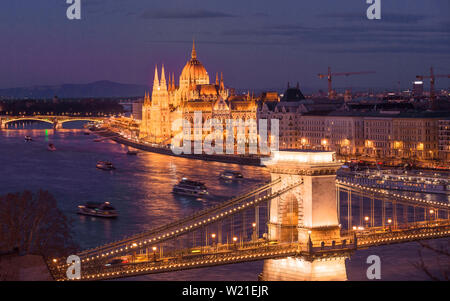 Stadtbild von Budapest mit hellen Parlament und Donau mit Brücke. Dunkle blau der Himmel spiegelt in Wasser nach Sonnenuntergang. Stockfoto