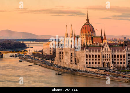 Stadtbild von Budapest mit hellen Parlament durch die letzten Sonnenstrahlen vor Sonnenuntergang und Donau mit Brücke beleuchtet. Rosa und Lila Farben des Himmels Stockfoto