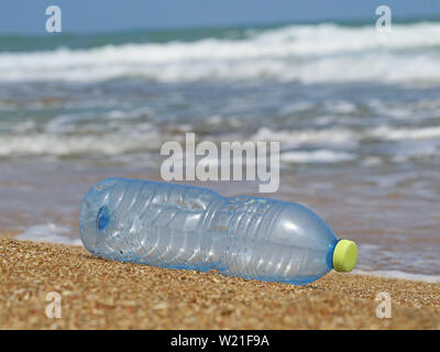 Kunststoff Flasche im Sand am Strand mit Wellen im Hintergrund, Konzept der Meeresverschmutzung durch Abfälle aus Kunststoffen Stockfoto