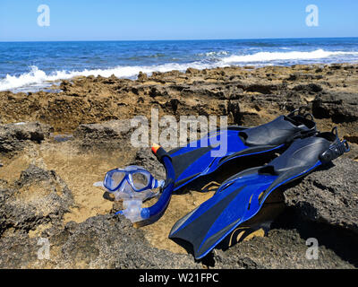 Blaue Flossen und Maske für Schnorcheln, Tauchen liegen am Meer mit Wellen und blauen Himmel im Hintergrund Stockfoto