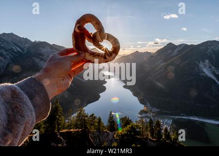 Hand, die Bayerische brezel vor Alpenpanorama Blick von Schonjochl, Plansee, Tirol, Österreich Stockfoto