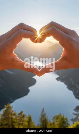 Hand bildet ein Herz vor der Alpen und Bergsee, Sun Star, Symbol der Liebe für die Natur und Wandern, Ansicht von Schonjochl, Plansee, Tirol, Österreich Stockfoto