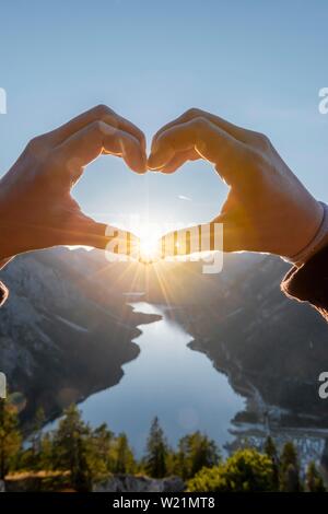 Hand bildet ein Herz vor der Alpen und Bergsee, Sun Star, Symbol der Liebe für die Natur und Wandern, Ansicht von Schonjochl, Plansee, Tirol, Österreich Stockfoto