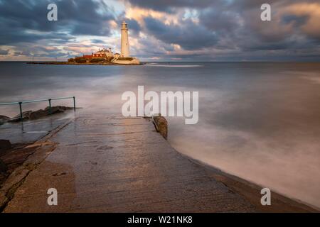 Leuchtturm, St. Mary's Leuchtturm mit gewaschen über Straße bei Flut mit dramatischen Wolken bei Sonnenuntergang, Küste von Tyne, Northumberland, Großbritannien Stockfoto