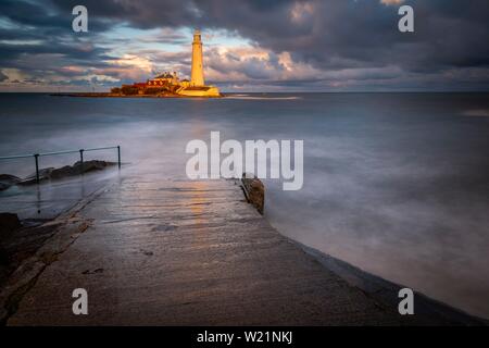 Leuchtturm, St. Mary's Leuchtturm mit gewaschen über Straße bei Flut mit dramatischen Wolken bei Sonnenuntergang, Küste von Tyne, Northumberland, Großbritannien Stockfoto