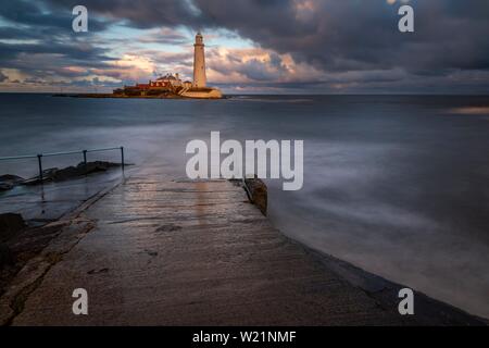 Leuchtturm, St. Mary's Leuchtturm mit gewaschen über Straße bei Flut mit dramatischen Wolken bei Sonnenuntergang, Küste von Tyne, Northumberland, Großbritannien Stockfoto