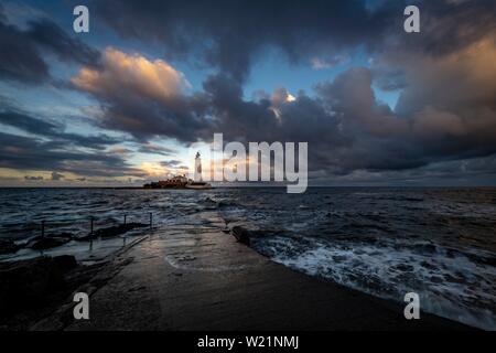 Leuchtturm, St. Mary's Leuchtturm mit gewaschen über Straße bei Flut mit dramatischen Wolken bei Sonnenuntergang, Küste von Tyne, Northumberland, Großbritannien Stockfoto