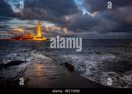 Leuchtturm, St. Mary's Leuchtturm mit gewaschen über Straße bei Flut mit dramatischen Wolken bei Sonnenuntergang, Küste von Tyne, Northumberland, Großbritannien Stockfoto