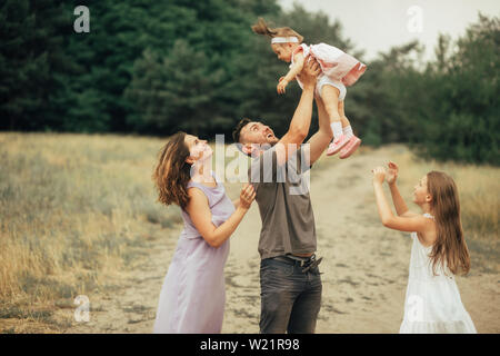 Glückliche Familie hat Spaß auf einem Weg und wirft ihre kleine Tochter in den Wald. Stockfoto